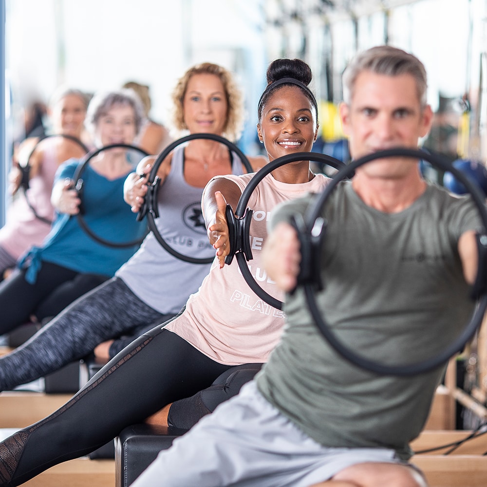 A line of Club Pilates members doing stretches with a Pilates Circle