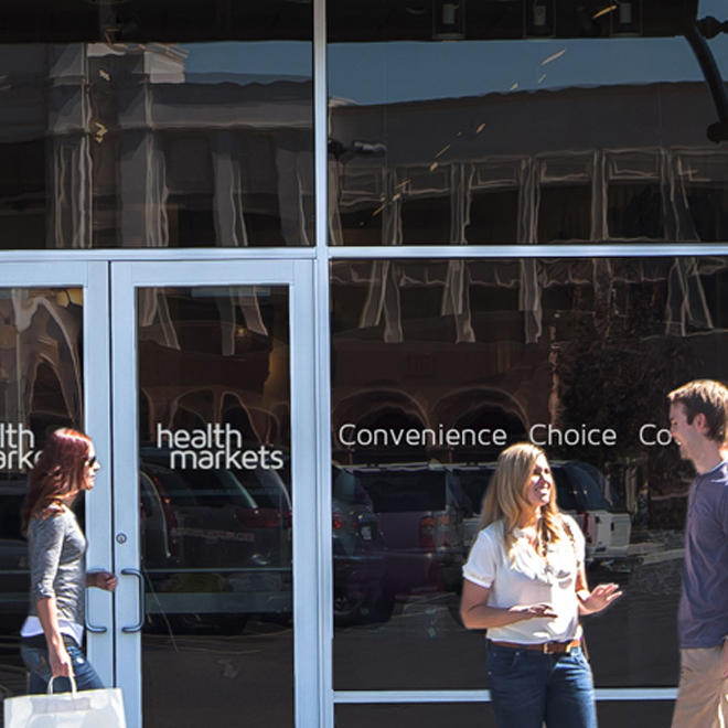A customer with a shopping bag, another couple stand outside a HealthMarkets location.